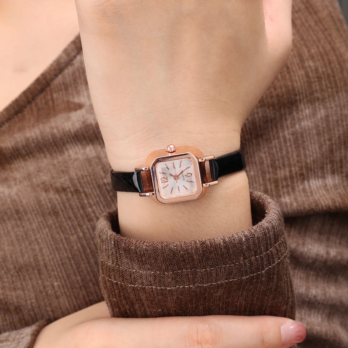 Relógio feminino com pulseira preta de couro e mostrador quadrado dourado.