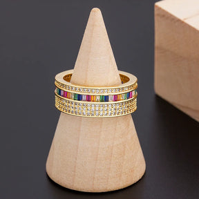 Anel dourado feminino com zircônias coloridas e detalhes cravejados, design delicado e elegante.