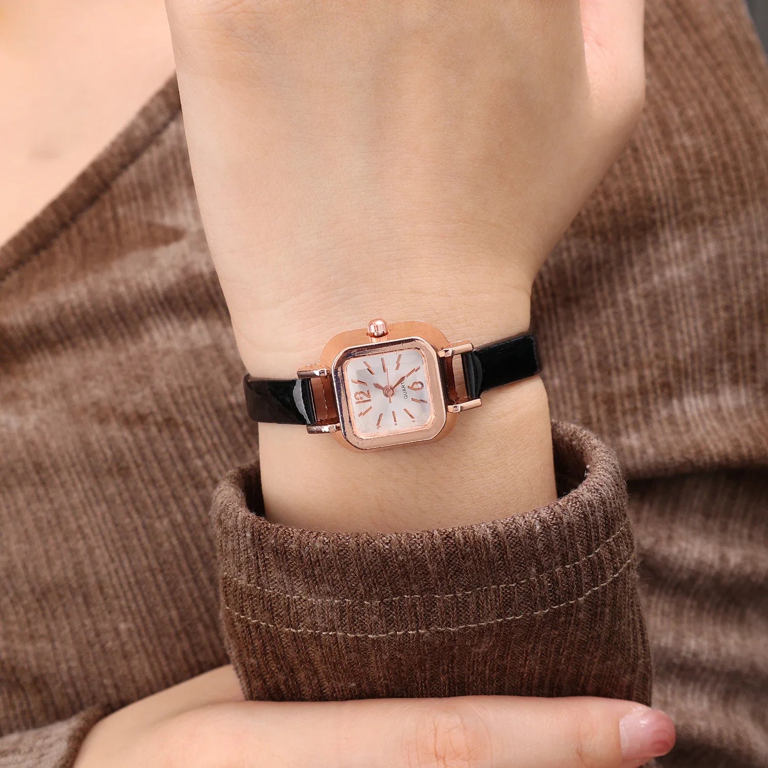 Relógio feminino com pulseira preta de couro e mostrador quadrado dourado.