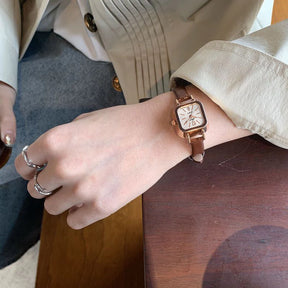 Relógio feminino Elegante com pulseira marrom de couro e mostrador quadrado dourado.