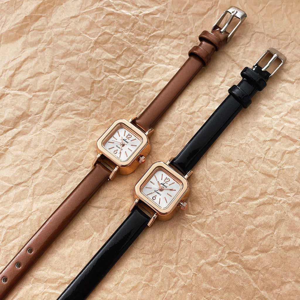 Relógio feminino com pulseira preta de couro e mostrador quadrado dourado.