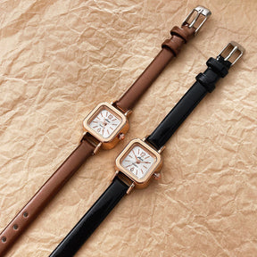 Relógio feminino com pulseira preta de couro e mostrador quadrado dourado.